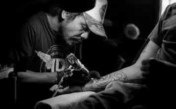 grayscale photo of man doing tattoo